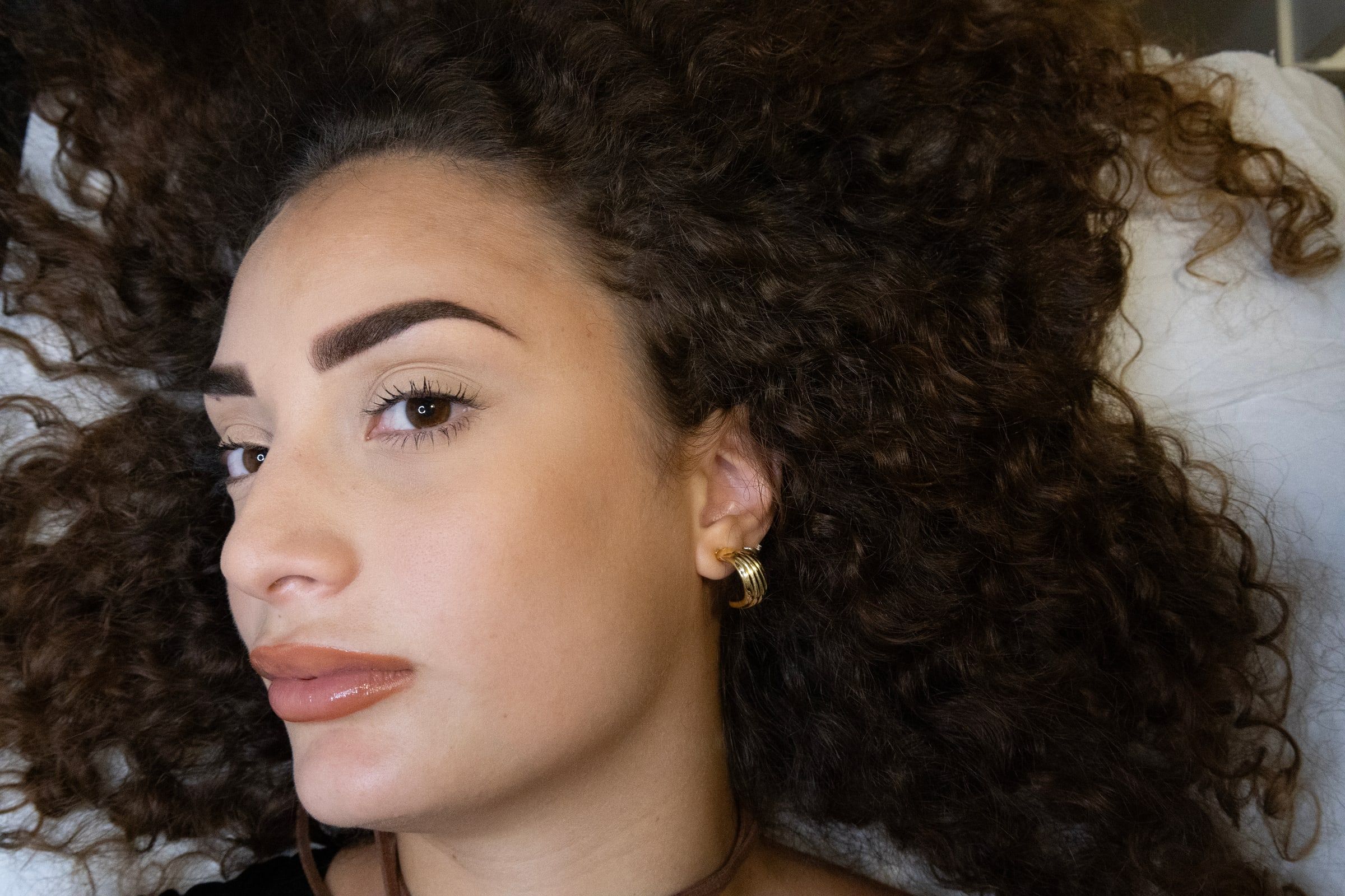 Viso di tre quarti con le sopracciglia appena pigmentate, i capelli ricci sul lenzuolo bianco